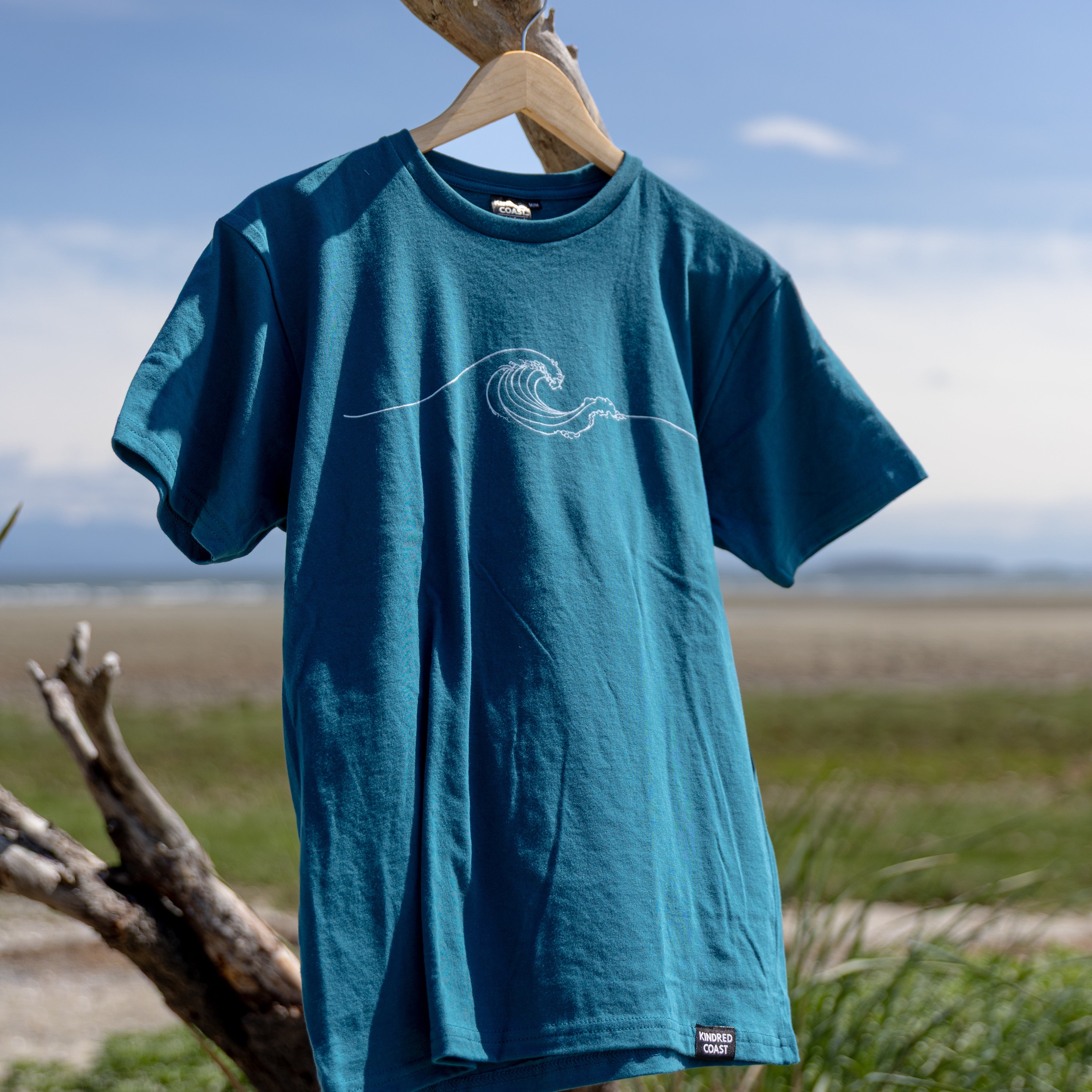 Blue t-shirt with a wave design on a wooden hanger against a natural background