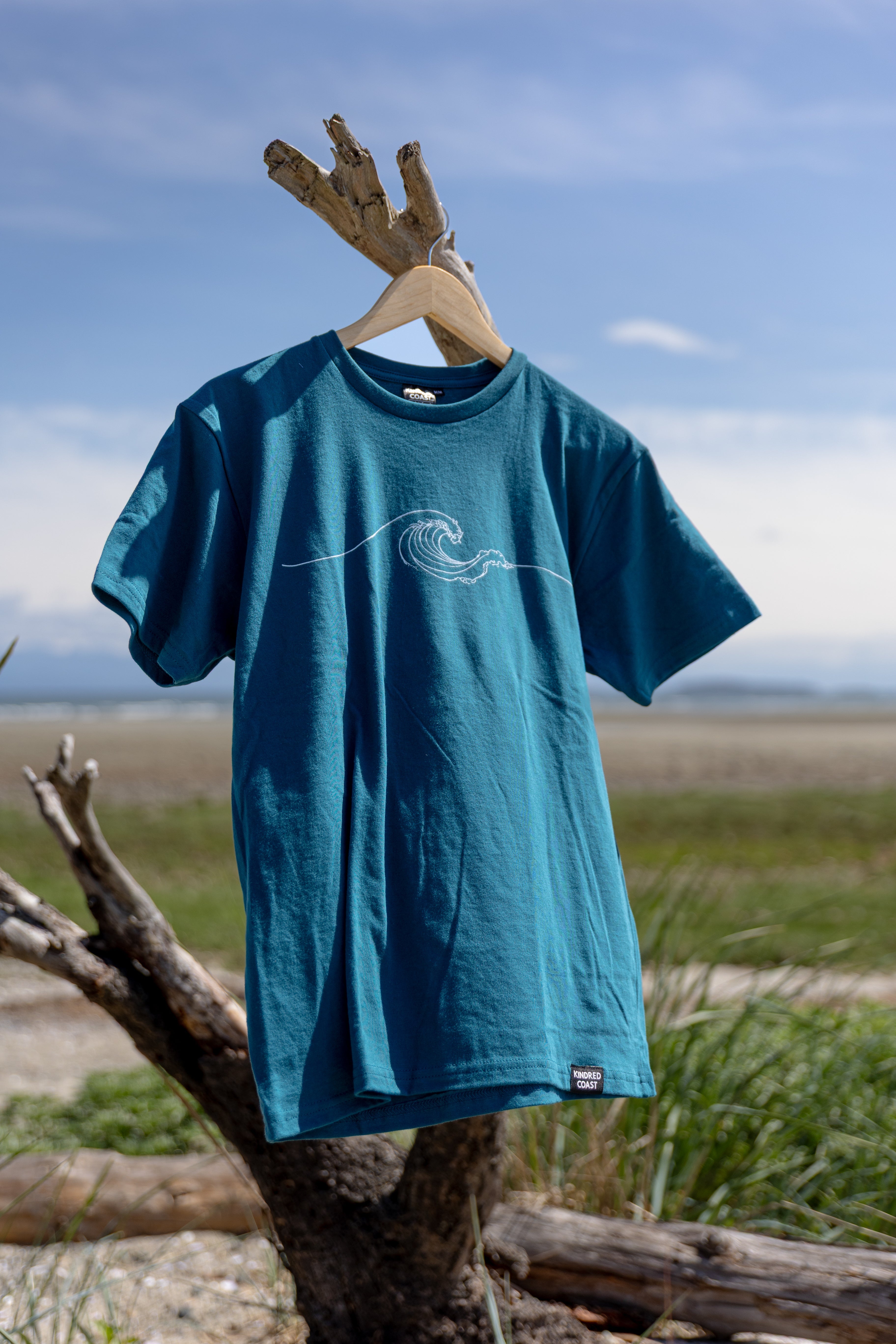 Blue t-shirt with a wave design on a wooden hanger against a natural background