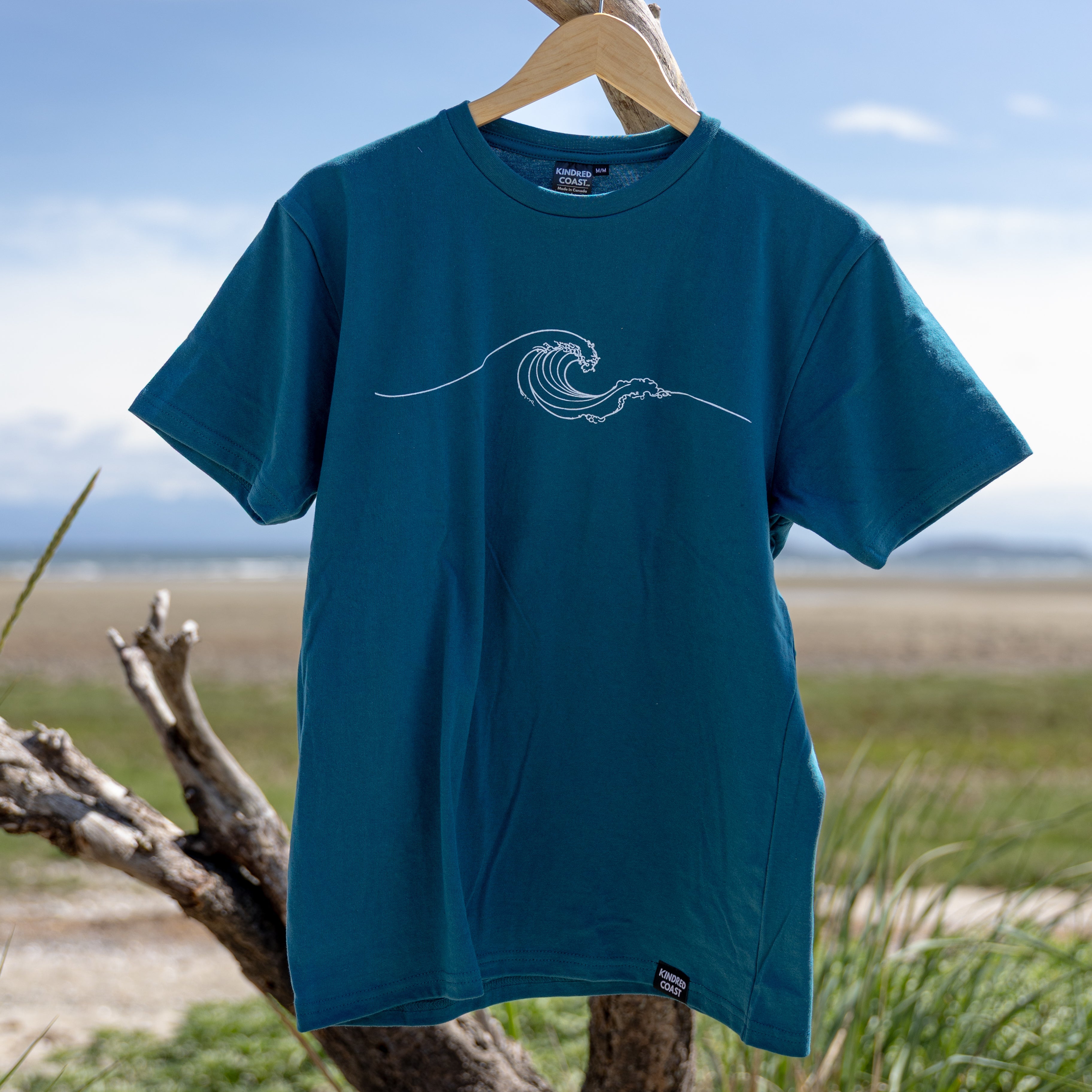 Blue t-shirt with a wave design on a wooden hanger against a natural background