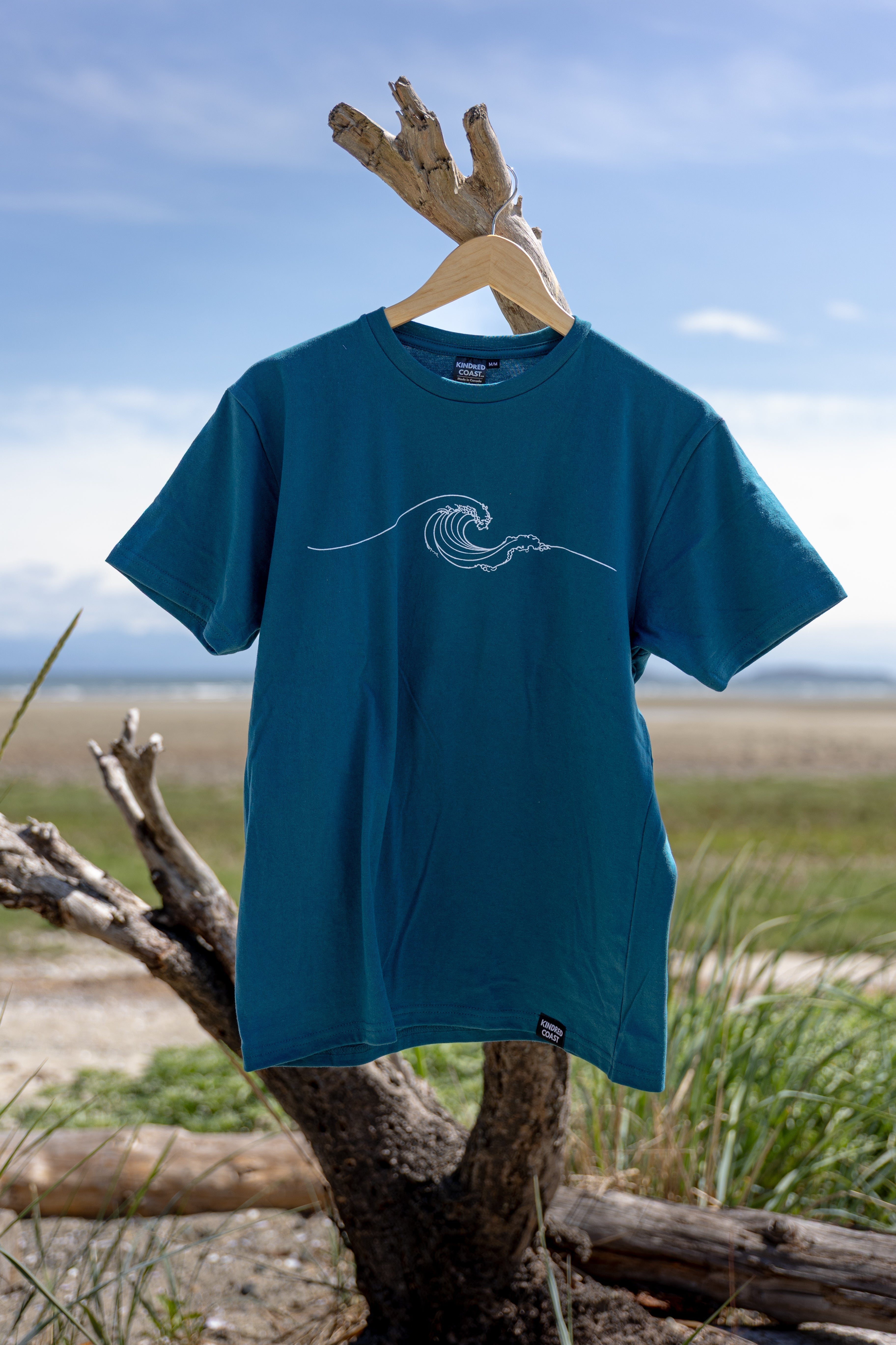 Blue t-shirt with a wave design on a wooden hanger against a natural background