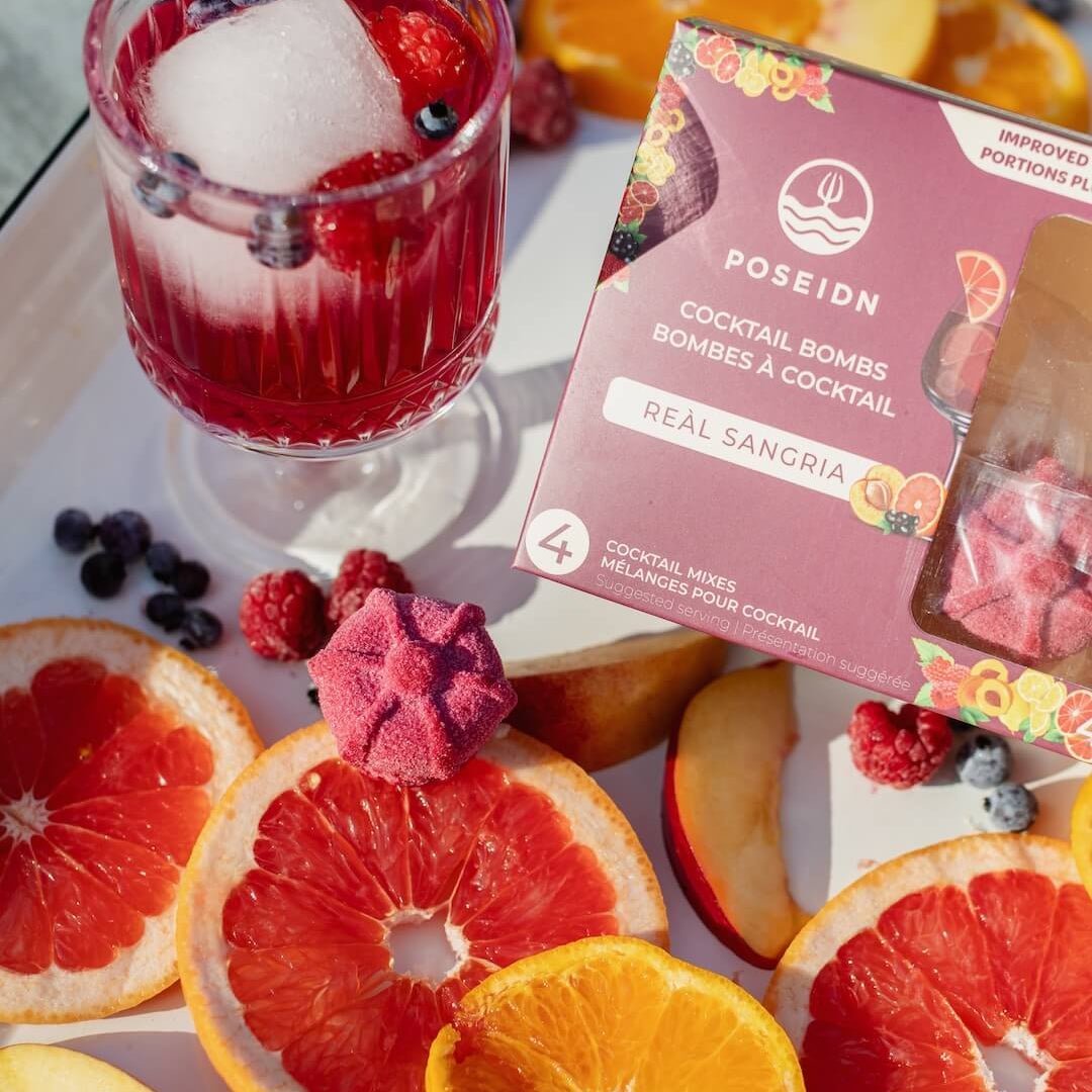 Cocktail with fruit slices and a box of Poseidn cocktail bombs on a white surface