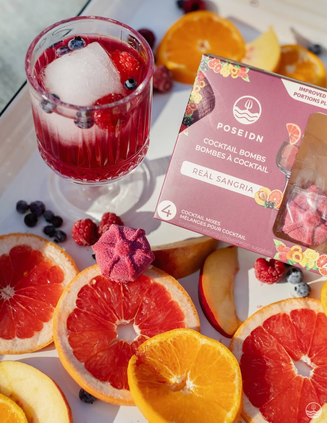 Cocktail with fruit slices and a box of Poseidn cocktail bombs on a white surface