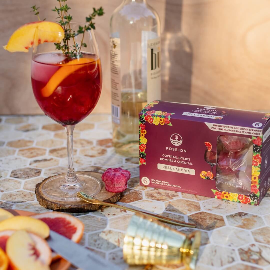Garnished cocktail with a bottle of white wine and a box of Pomegranate cocktails on a patterned surface.