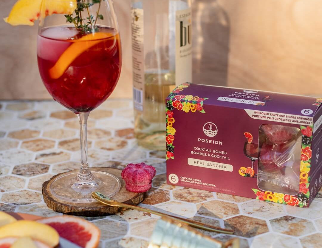 Garnished cocktail with a bottle of white wine and a box of Pomegranate cocktails on a patterned surface.