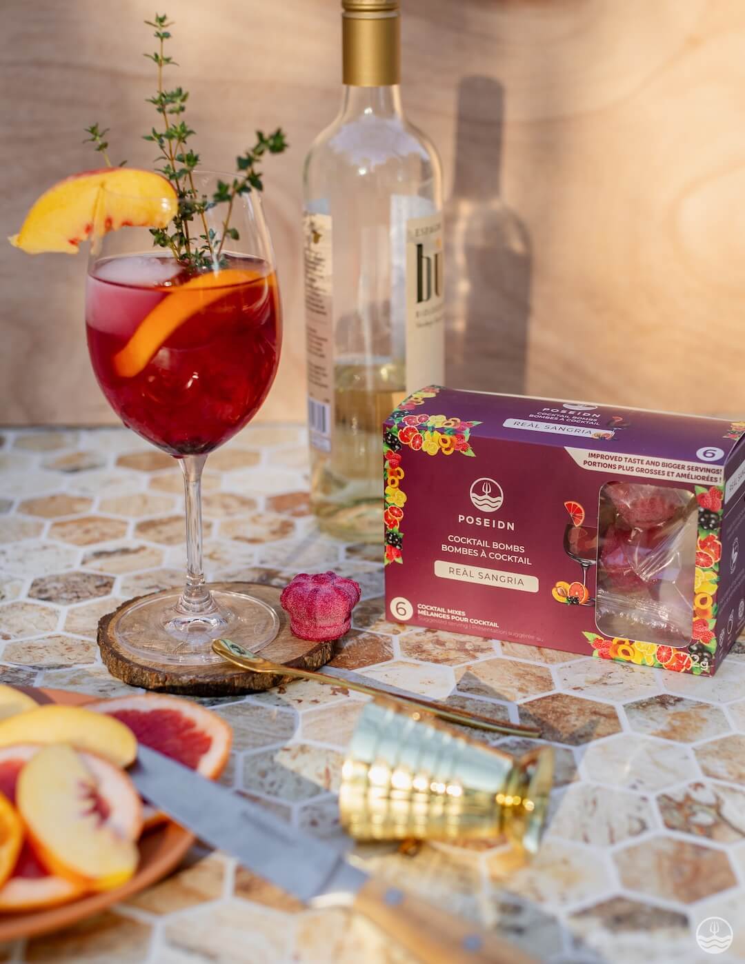 Garnished cocktail with a bottle of white wine and a box of Pomegranate cocktails on a patterned surface.
