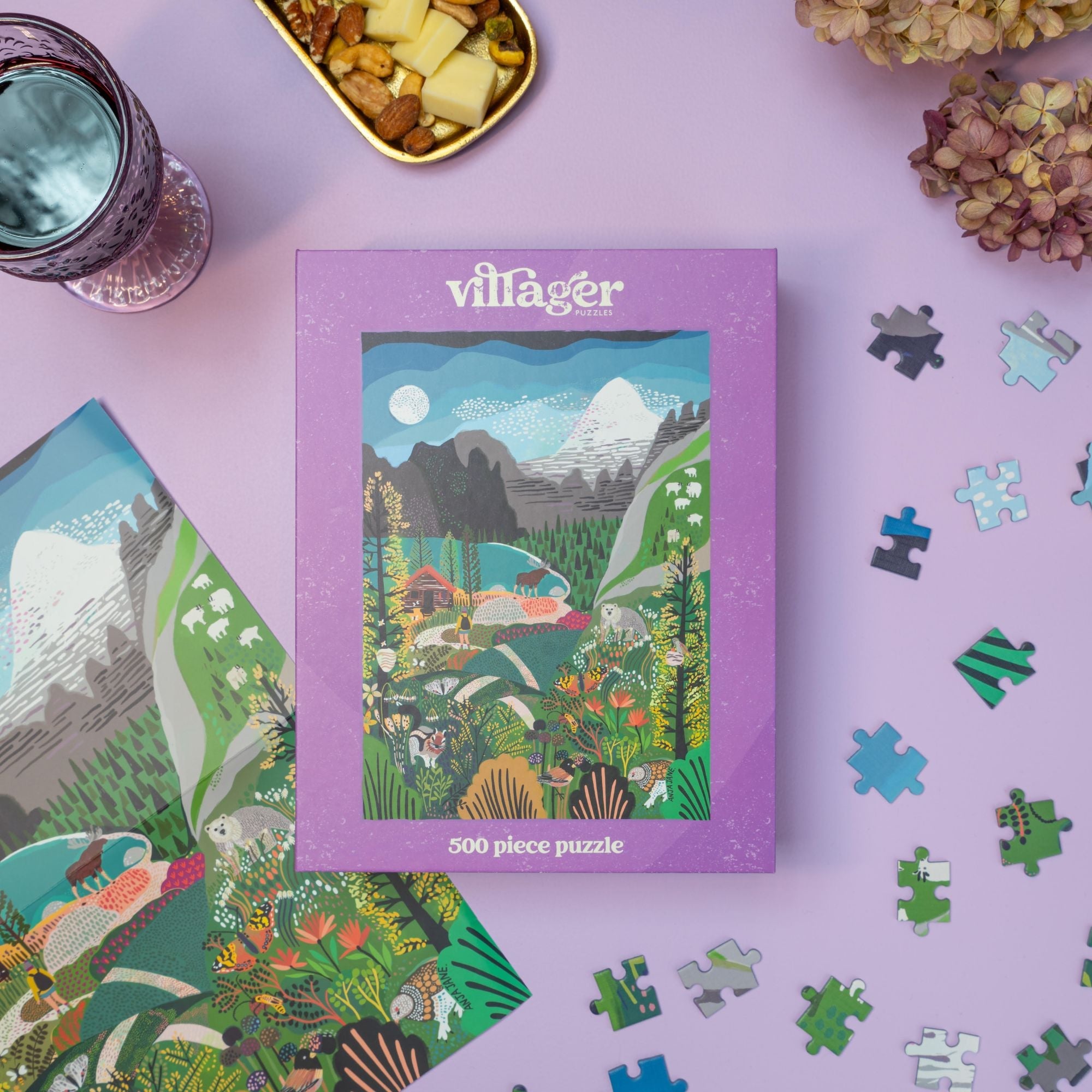 Rockies Explorer | 500-Piece Puzzle for Adults Villager puzzle box with a scenic design on a pink surface with puzzle pieces scattered around.