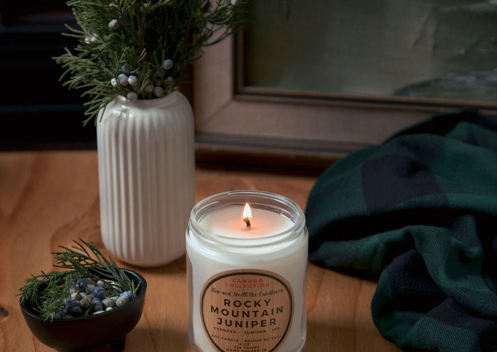 Stopandsmellthecandles Rocky Mountain Juniper soy candle – 8 oz clear glass jar, lit beside juniper branches
