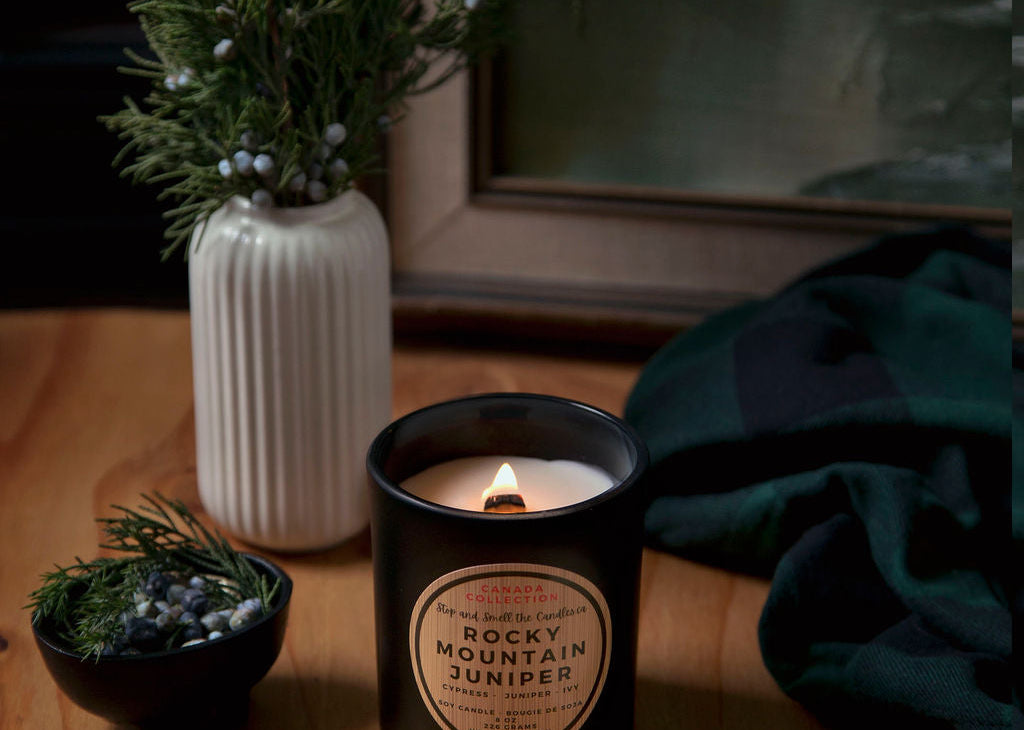 Candle with decorative packaging on a wooden surface, surrounded by plants and a towel.
