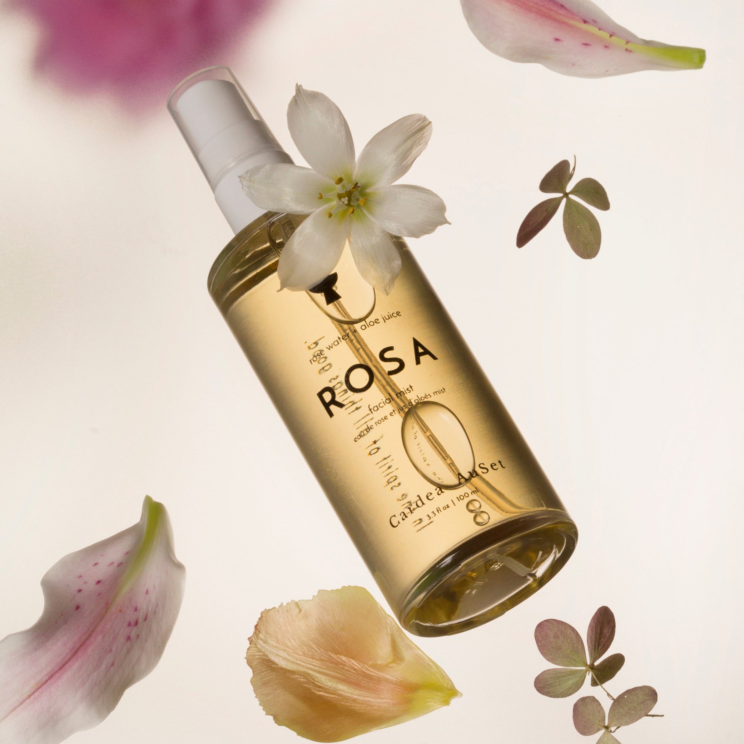 Gold bottle labeled 'ROSA' with flowers and leaves on a light background