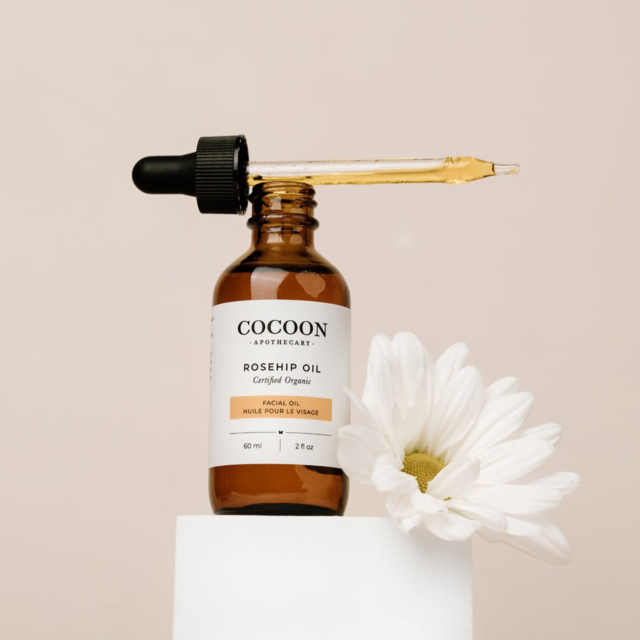 Cocoon Apothecary rosehip oil bottle with dropper on a beige background
