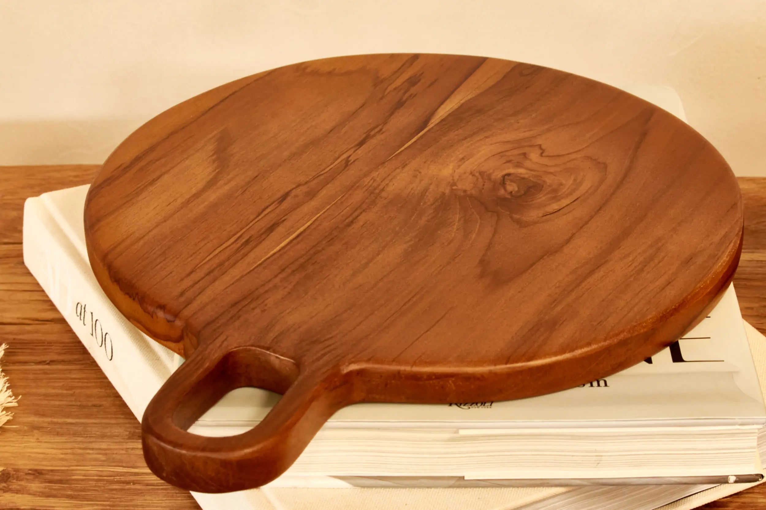 Wooden teak cutting board with handle on top of books