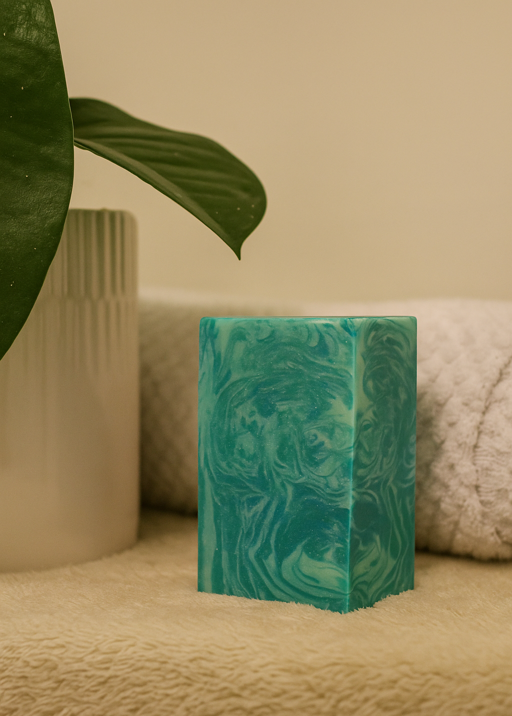 Green marbled candle on a textured surface with a plant leaf in the corner