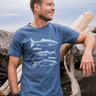 Man wearing a blue t-shirt with fish graphics, standing outdoors near wooden logs.