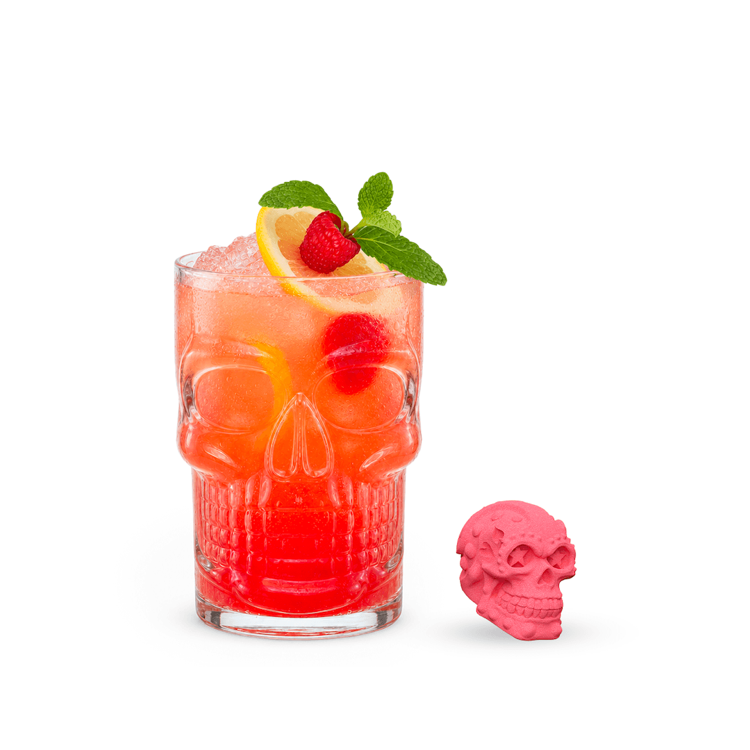 Skull-shaped cocktail glass with a colorful drink, lemon, raspberry, and mint on a white background