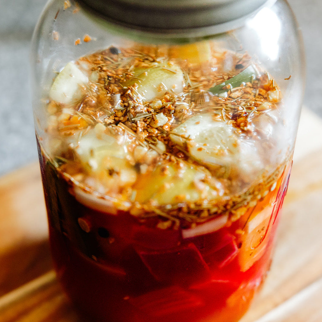 Glass jar with a red liquid and floating herbs on a wooden surface