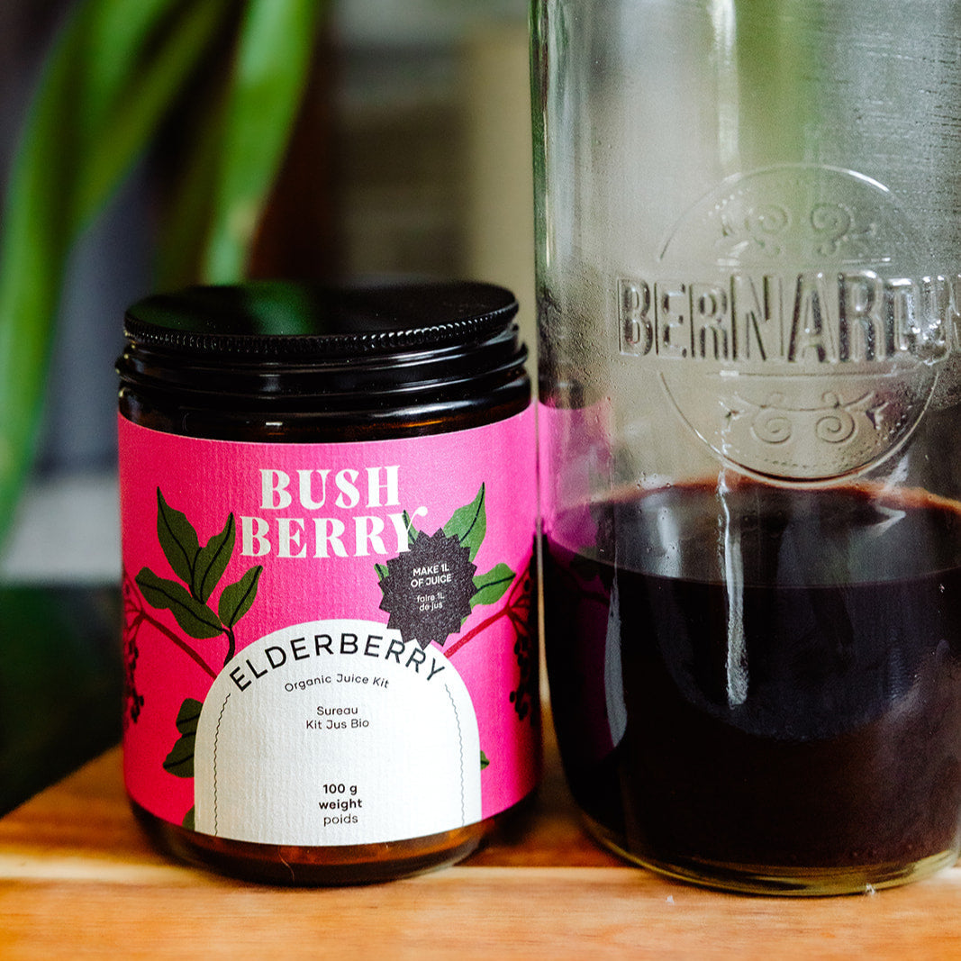 Jar of Bush Berry Elderberry juice kit next to a bottle of juice on a wooden surface.
