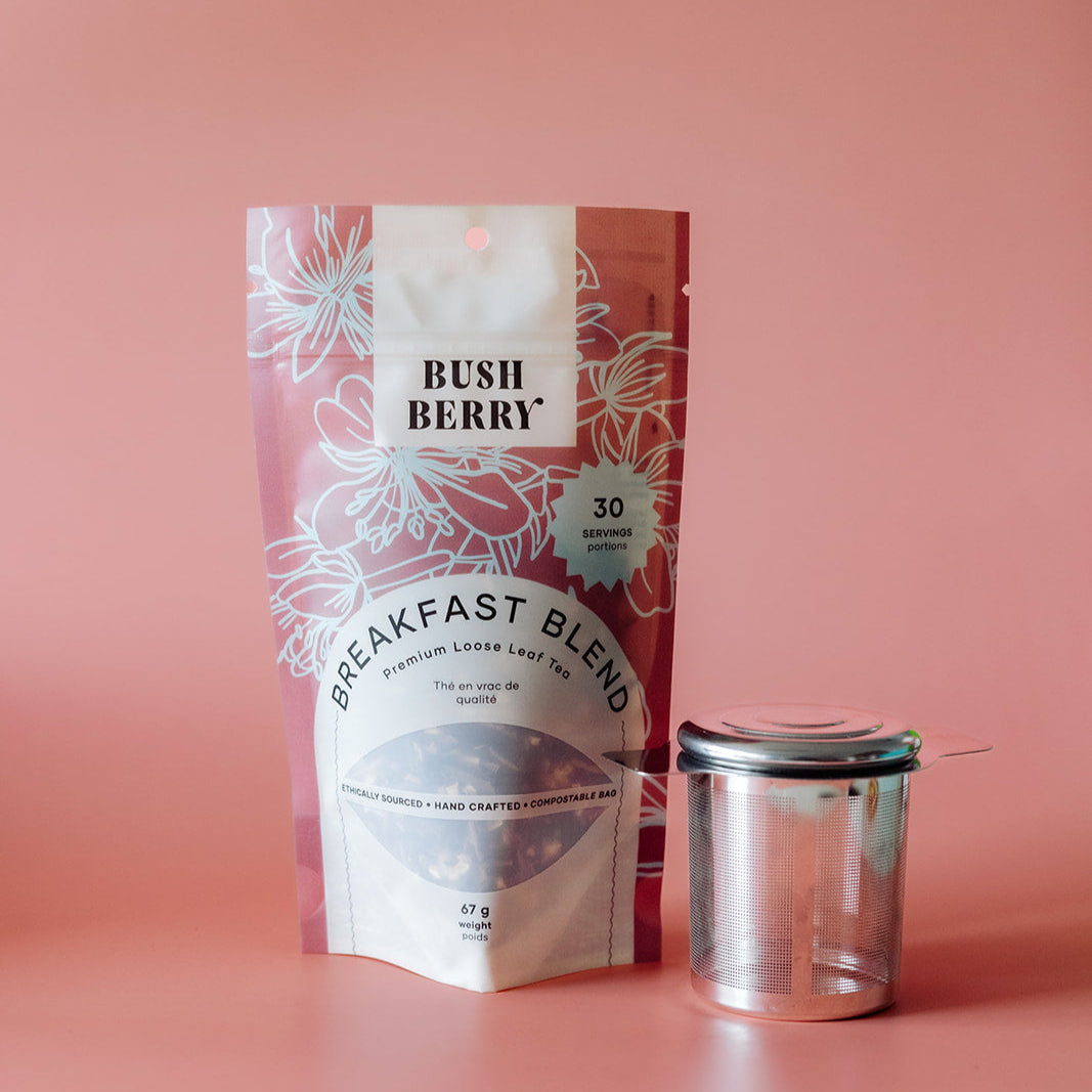 Tea package labeled 'Bush Berry Breakfast Blend' with a clear tea strainer on a pink background