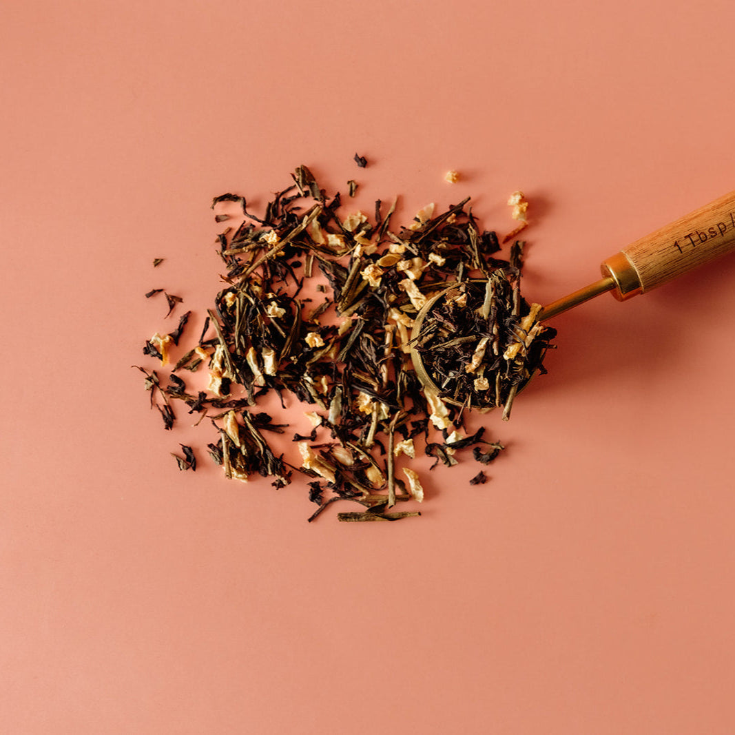 Tea leaves spilling from a wooden spoon on a pink background Organic Breakfast Blend Tea