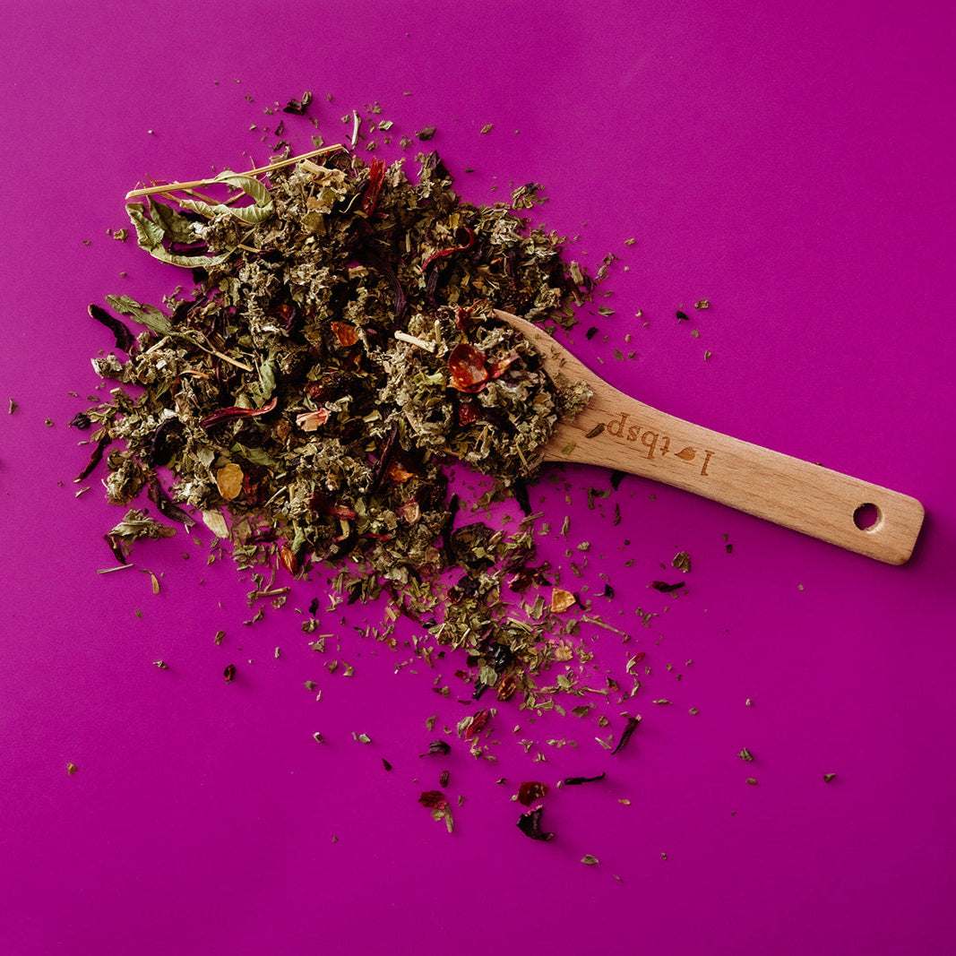 Wooden scoop with dried herbs on a pink background Organic Wild Raspberry Hibiscus Tea