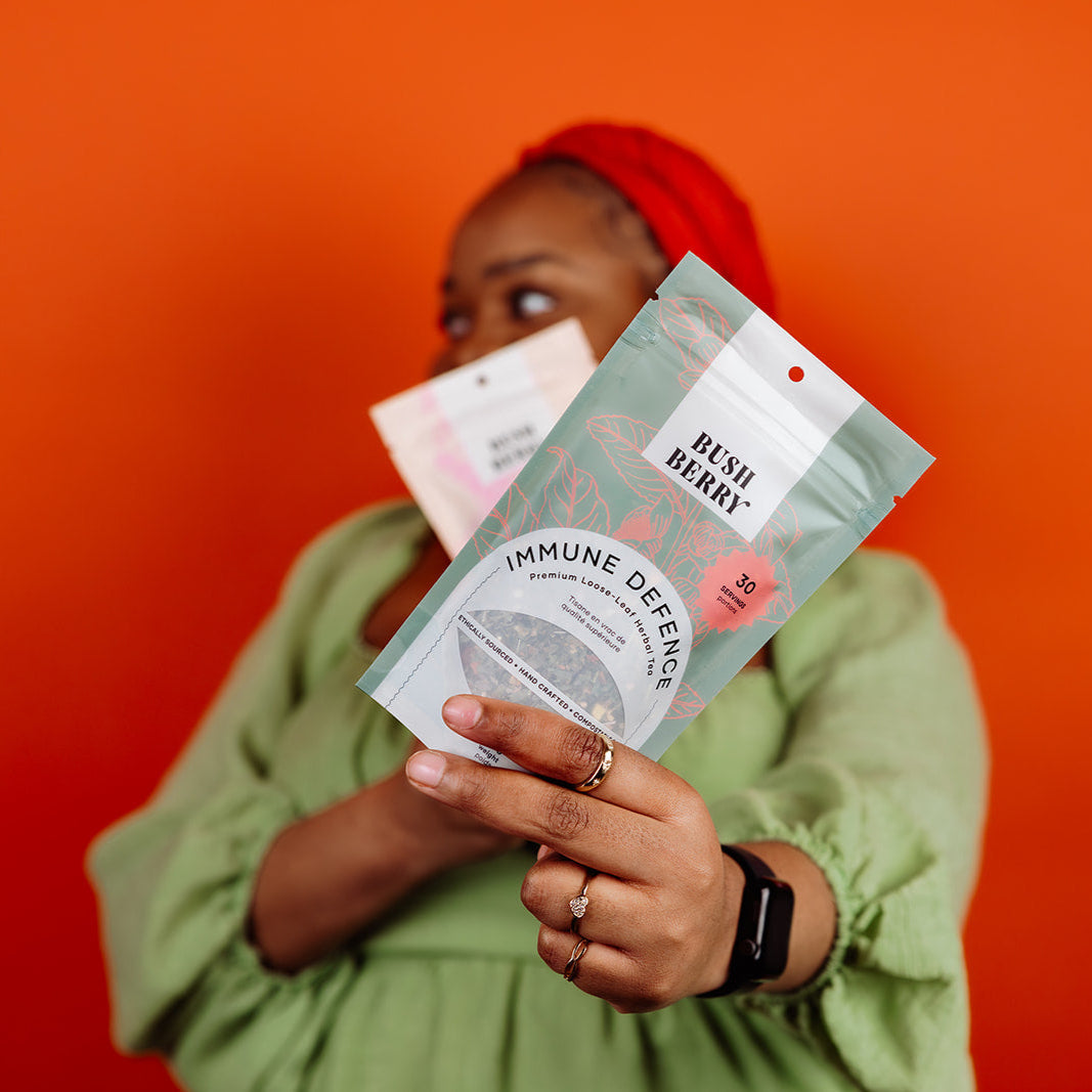 Person holding 'Bush & Berries Immune Defense' tea packages against an orange background