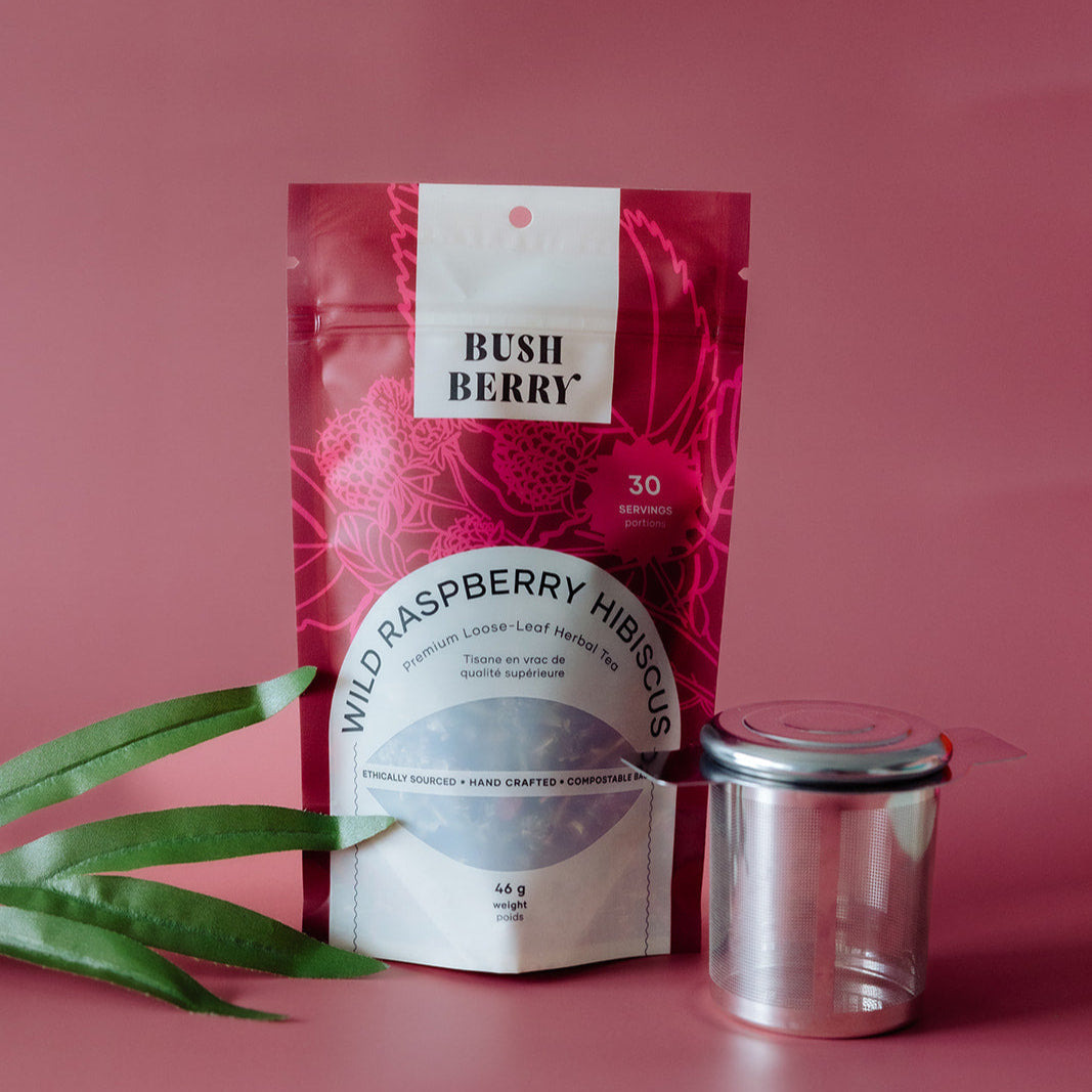 Tea package labeled 'Wild Raspberry Hibiscus' by Bush Berry on a pink background with a glass jar.