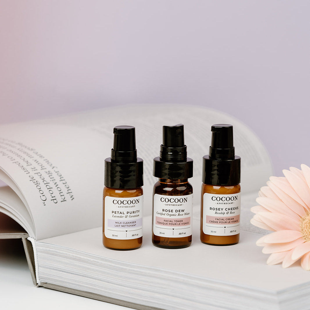 Three small bottles of Cocoon skincare products on an open book with a flower.
