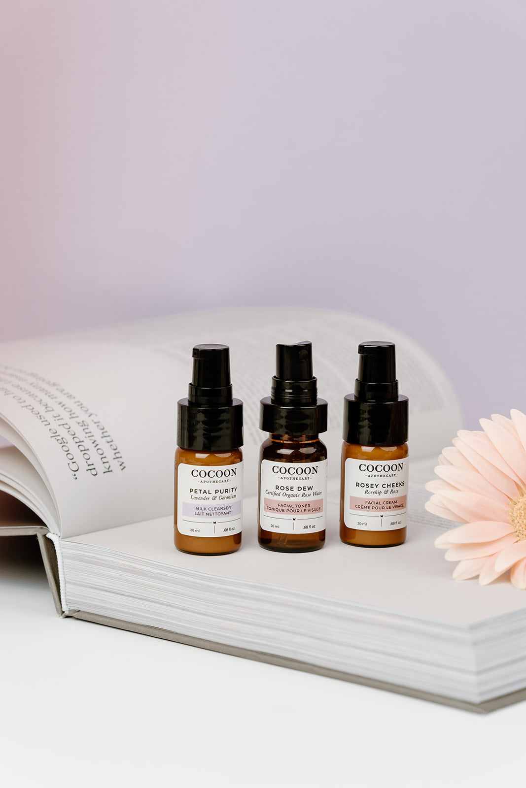 Three small bottles of Cocoon skincare products on an open book with a flower.