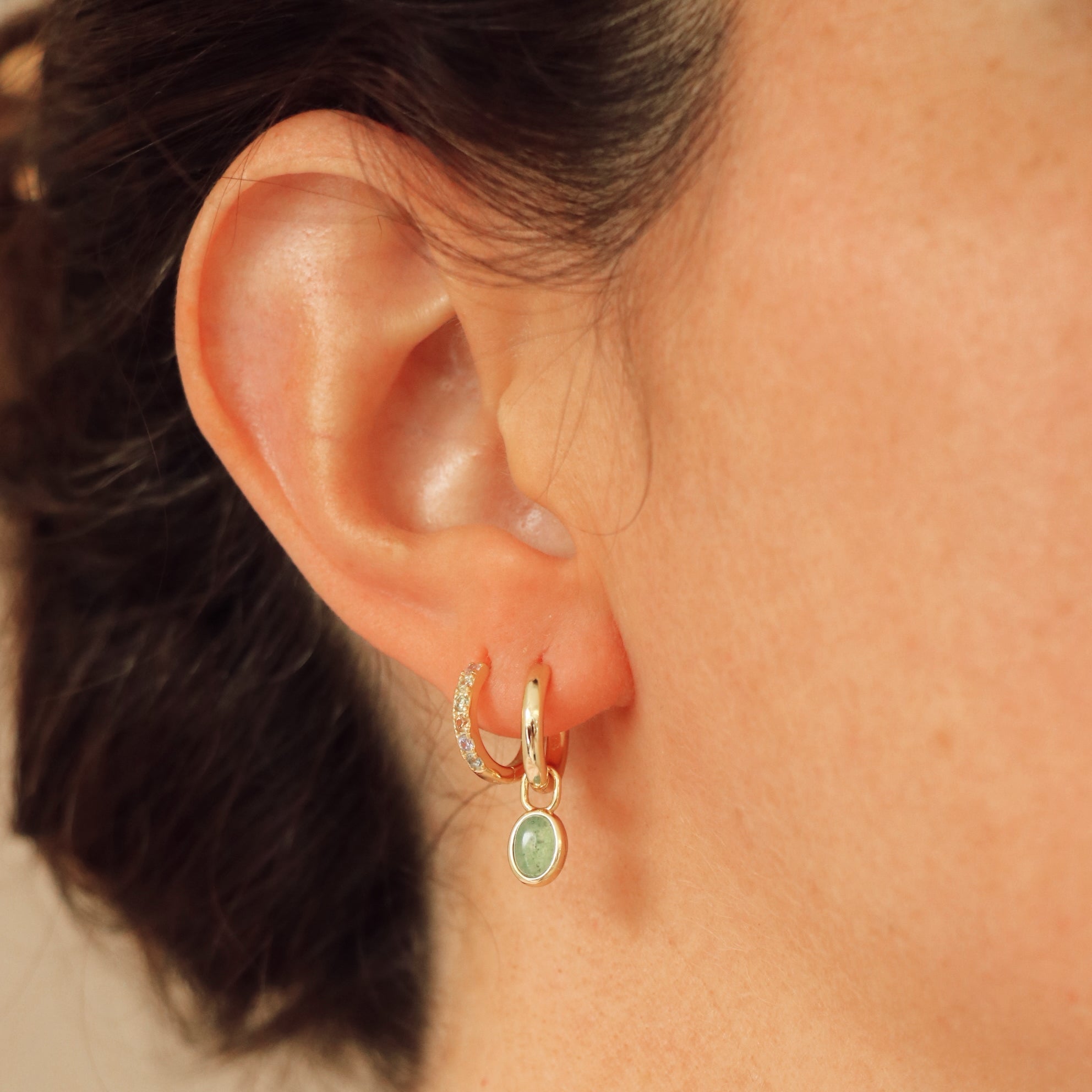 Close-up of an ear wearing a gold hoop earring with a green gemstone.
