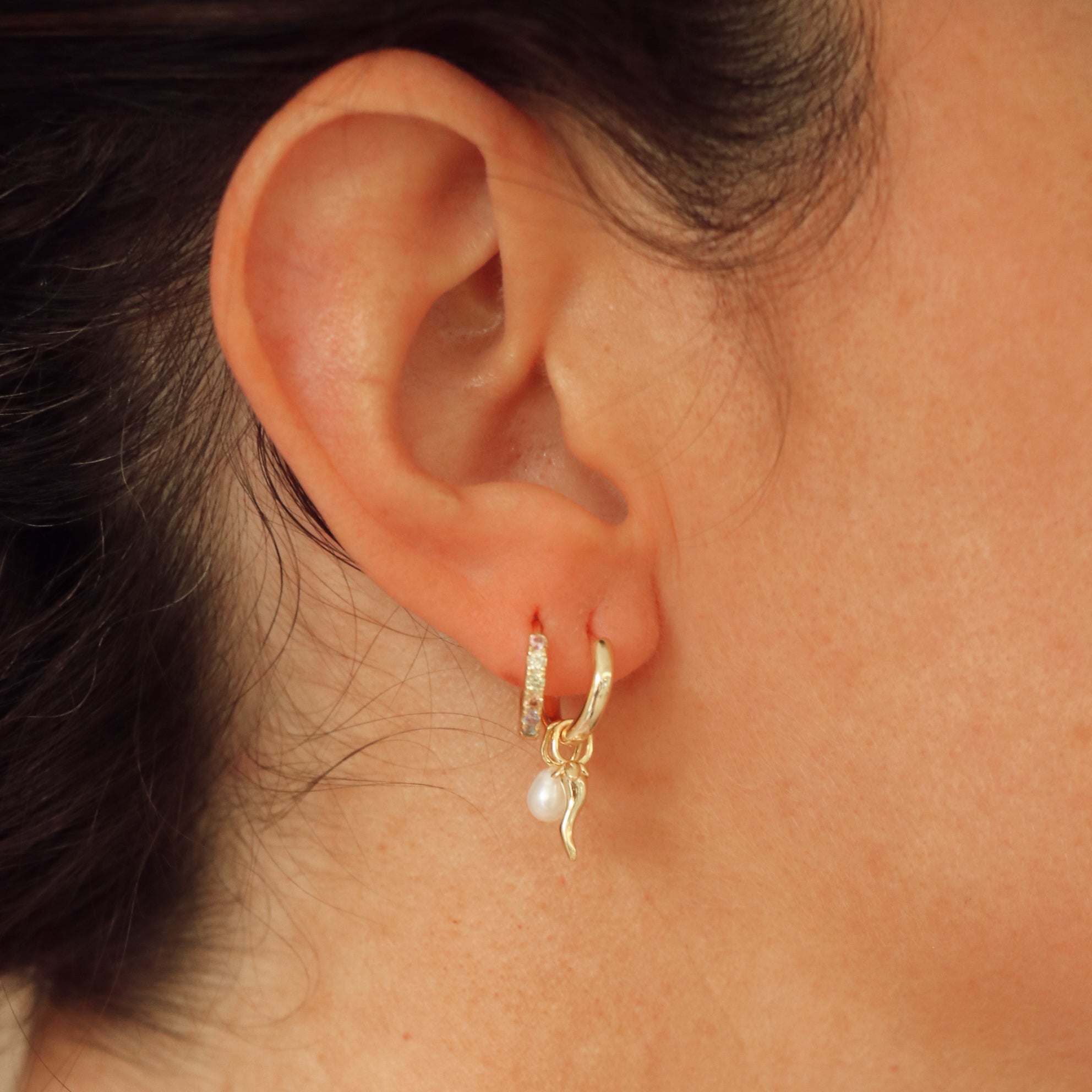 Close-up of an ear wearing a gold hoop earring with a pearl accent.