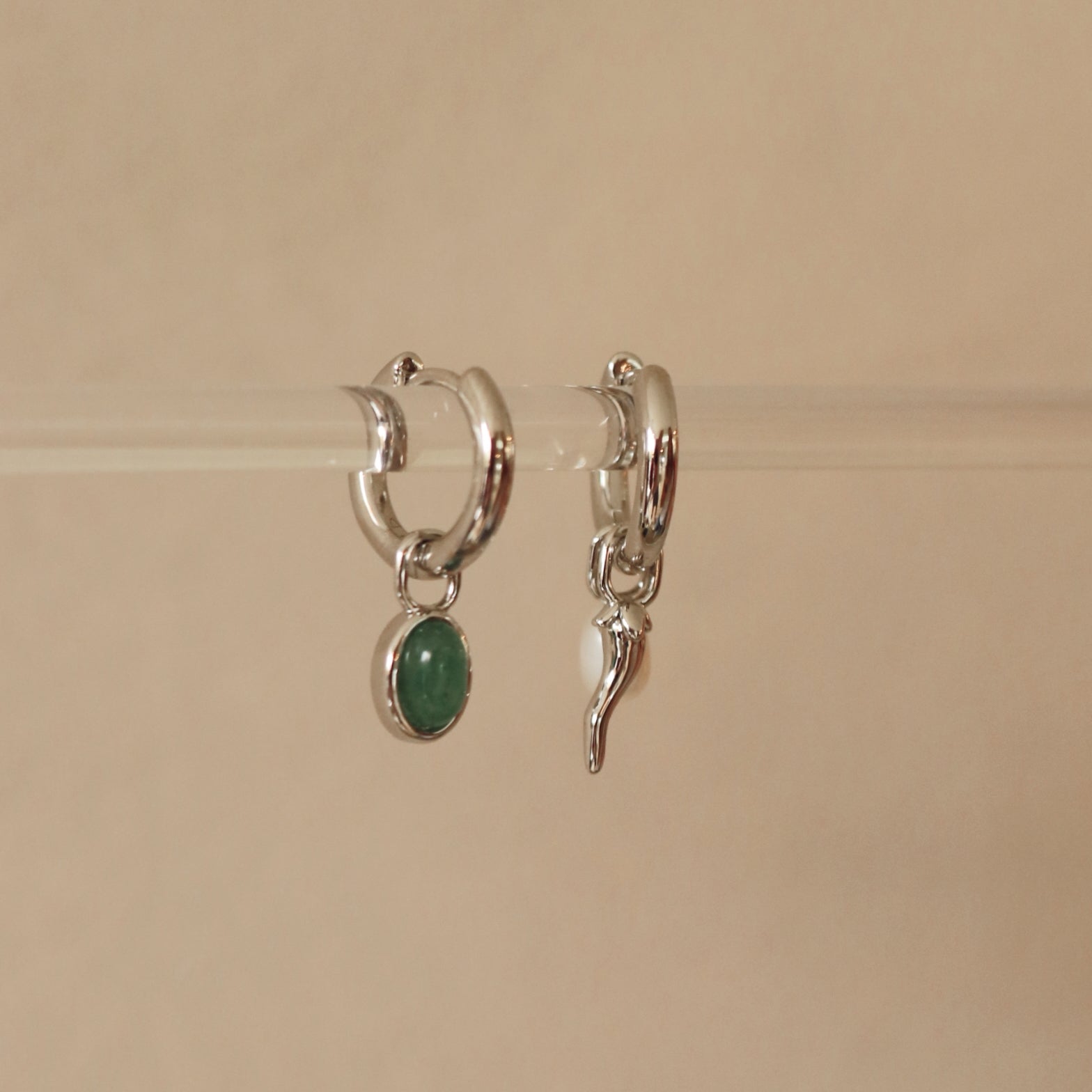 Silver hoop earrings with green gemstone and leaf charm on a beige background