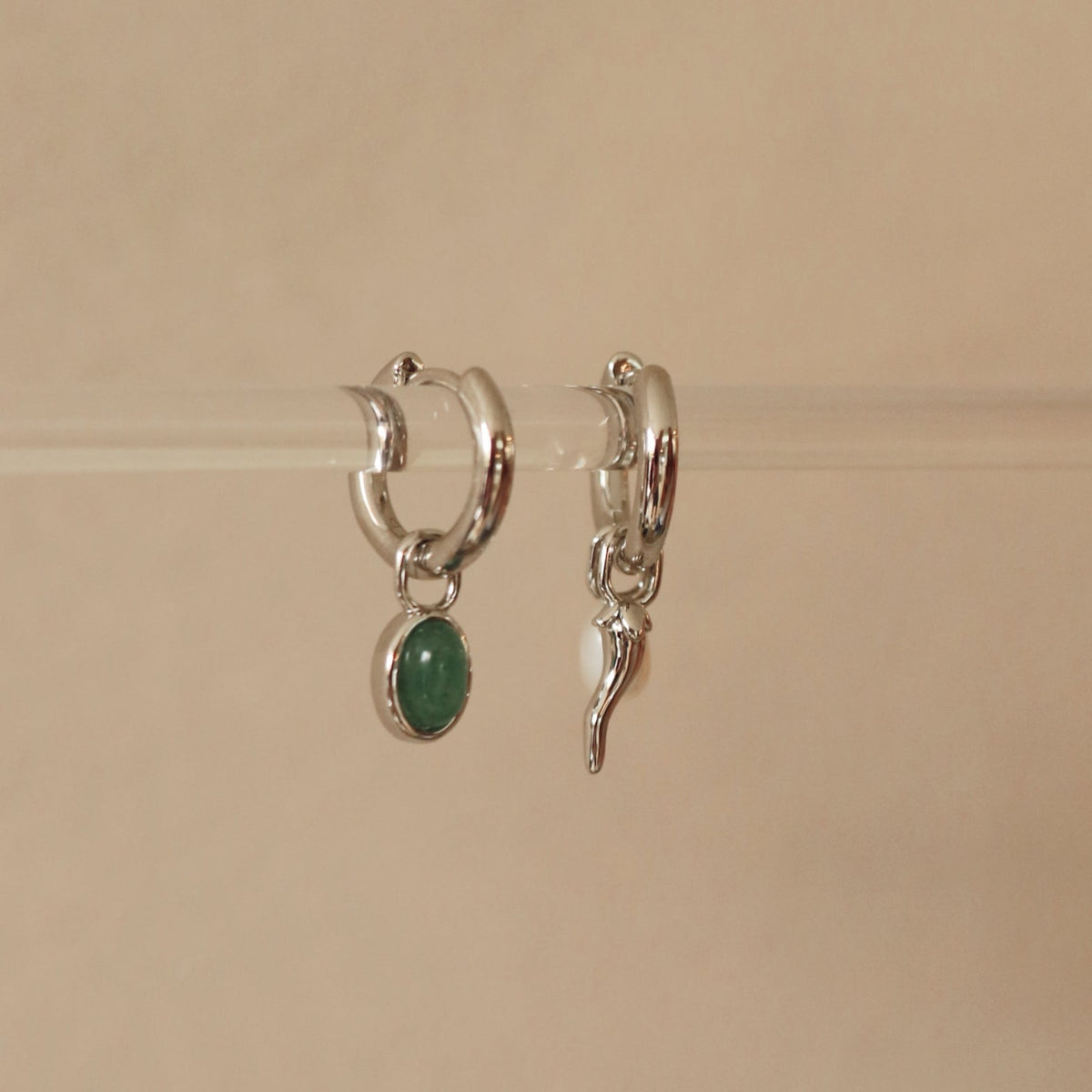 Silver hoop earrings with green gemstone and leaf charm on a beige background