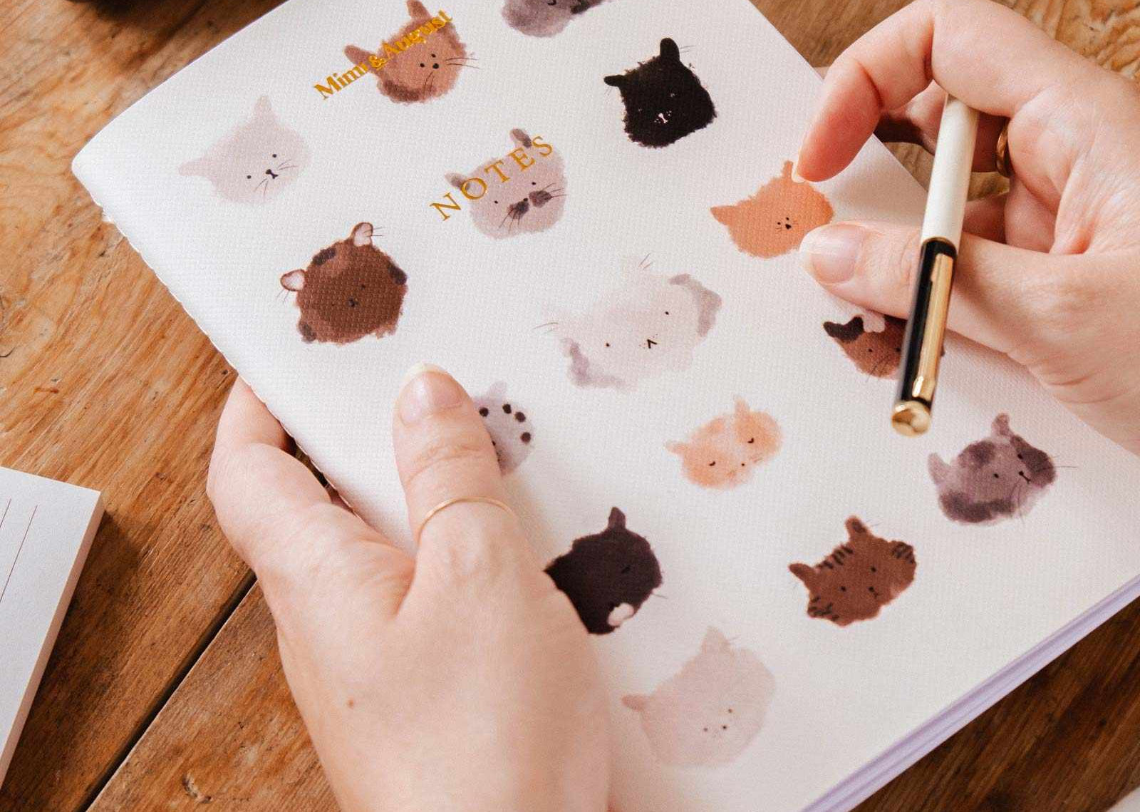 Person holding a notebook with animal stickers on a wooden table mimi-and-august