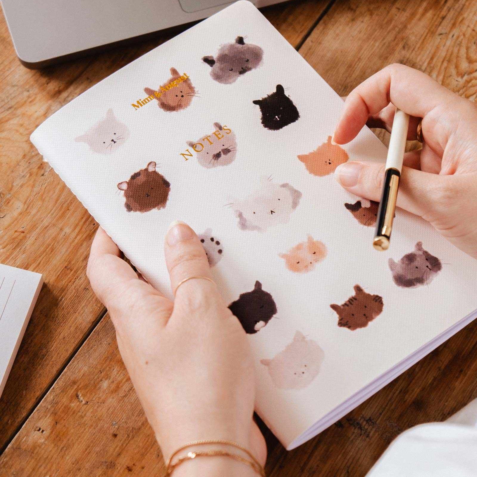 Person holding a notebook with animal stickers on a wooden table mimi-and-august