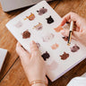 Person holding a notebook with animal stickers on a wooden table mimi-and-august