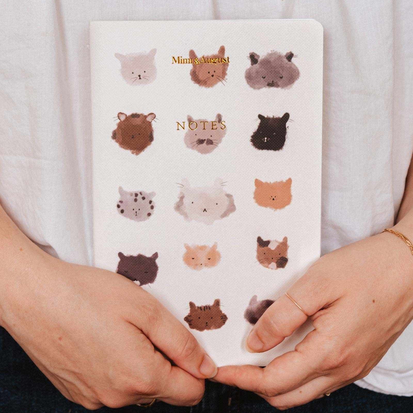 Notebook with animal face patterns held by a person wearing a white shirt. mimi-and-august