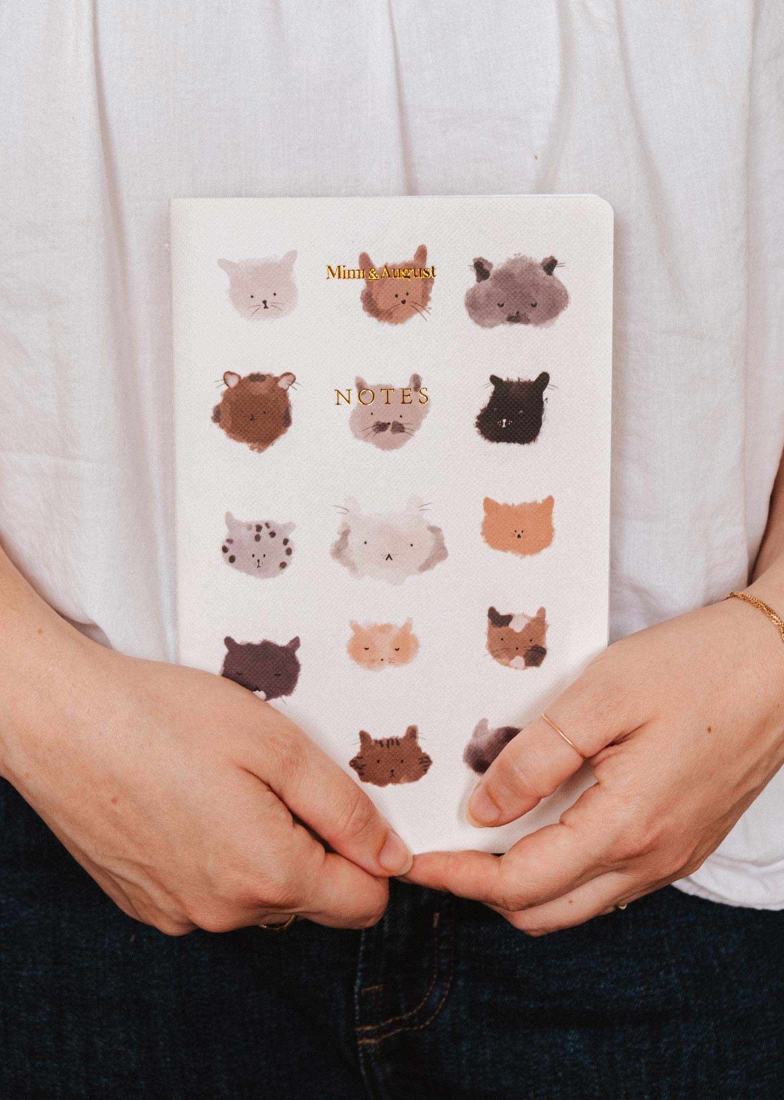 Notebook with animal face patterns held by a person wearing a white shirt. mimi-and-august