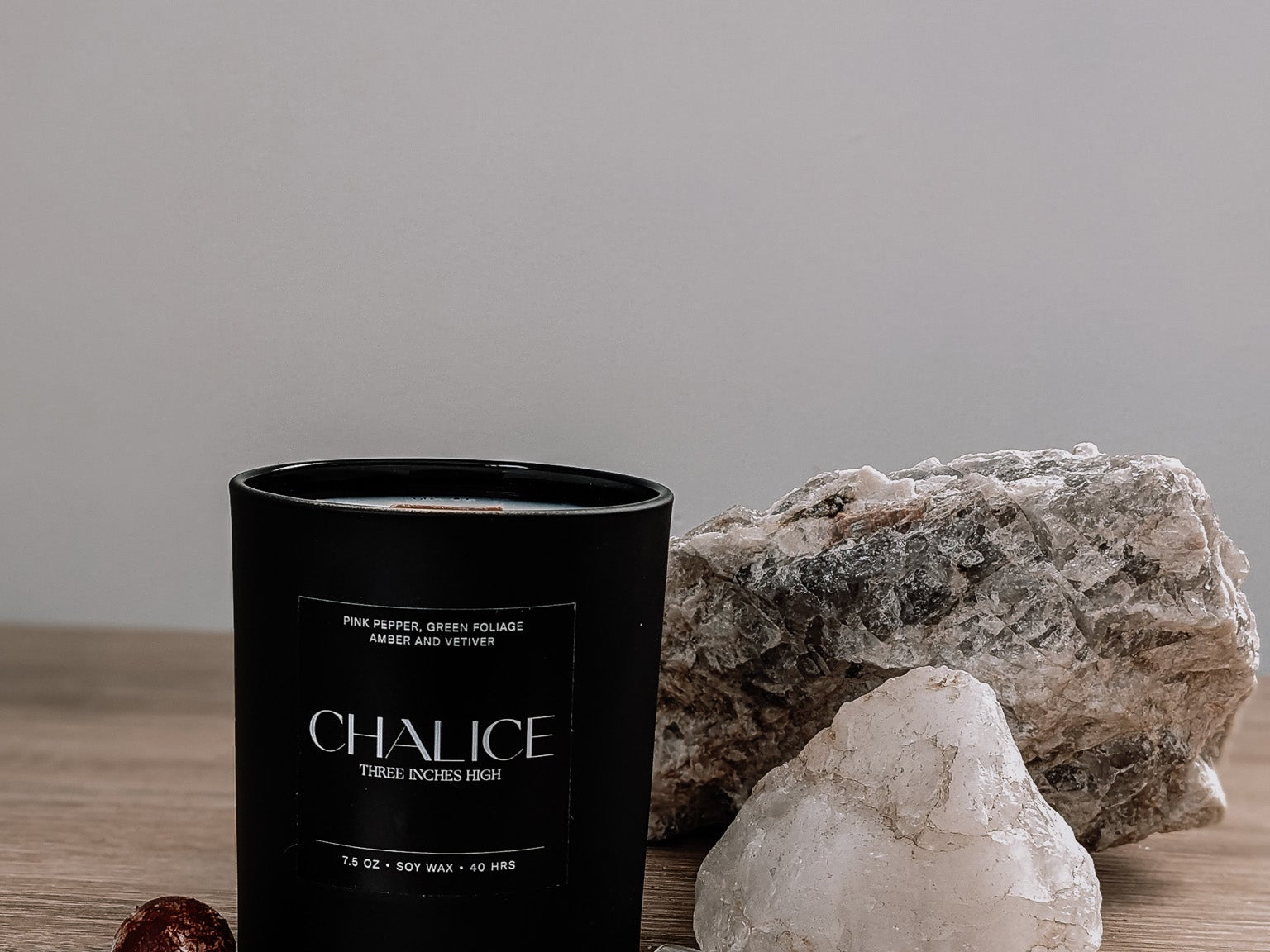 Black candle labeled 'Chalice' on a wooden surface with rocks and crystals.
