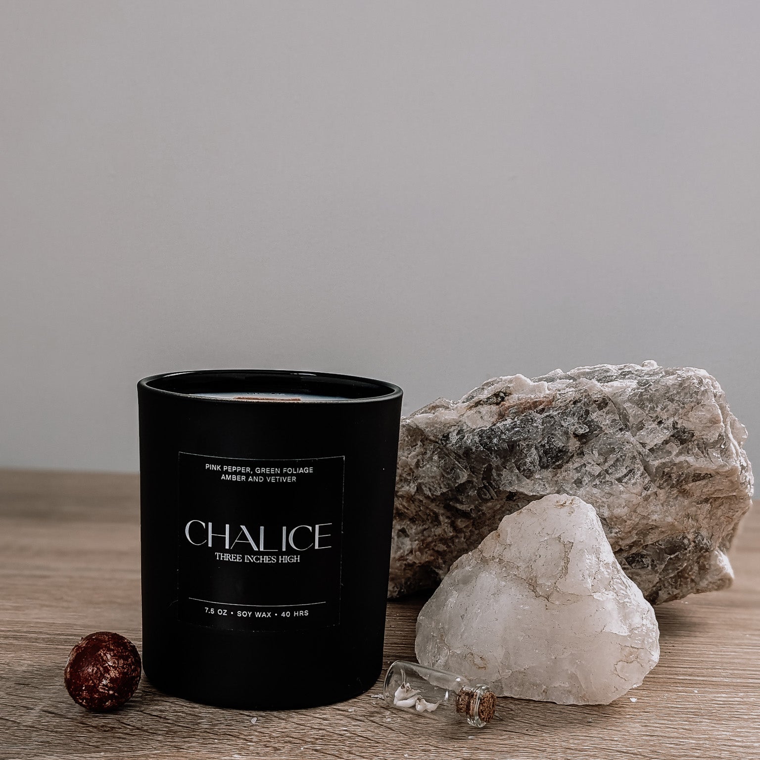 Black candle labeled 'Chalice' on a wooden surface with rocks and crystals.
