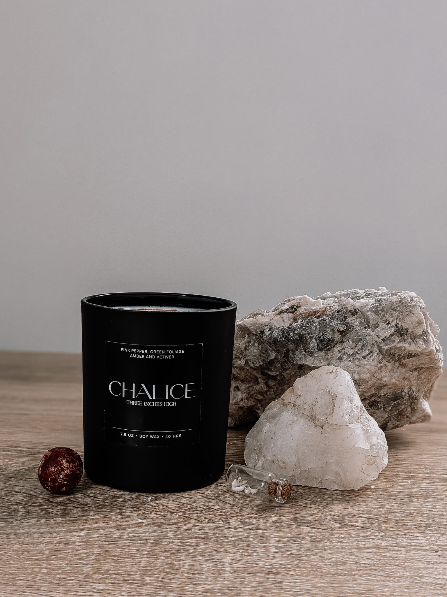 Black candle labeled 'Chalice' on a wooden surface with rocks and crystals.