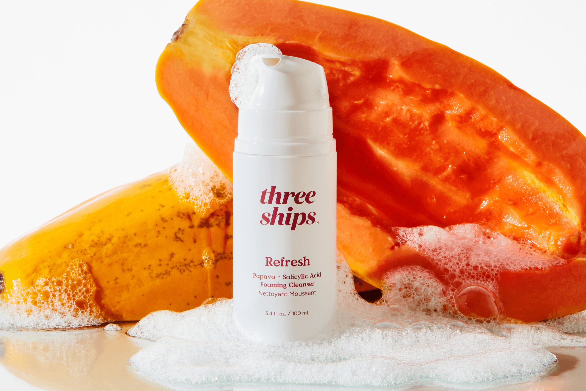 Bottle of Refresh Papaya + Salicylic Acid Cleanser with papaya slices, highlighting skin smoothness and freshness.