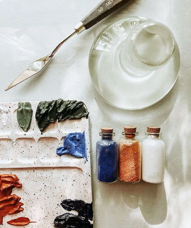 Art supplies including a palette, Clear Glass Paint Muller, paintbrush, and small bottles of paint on a textured surface.