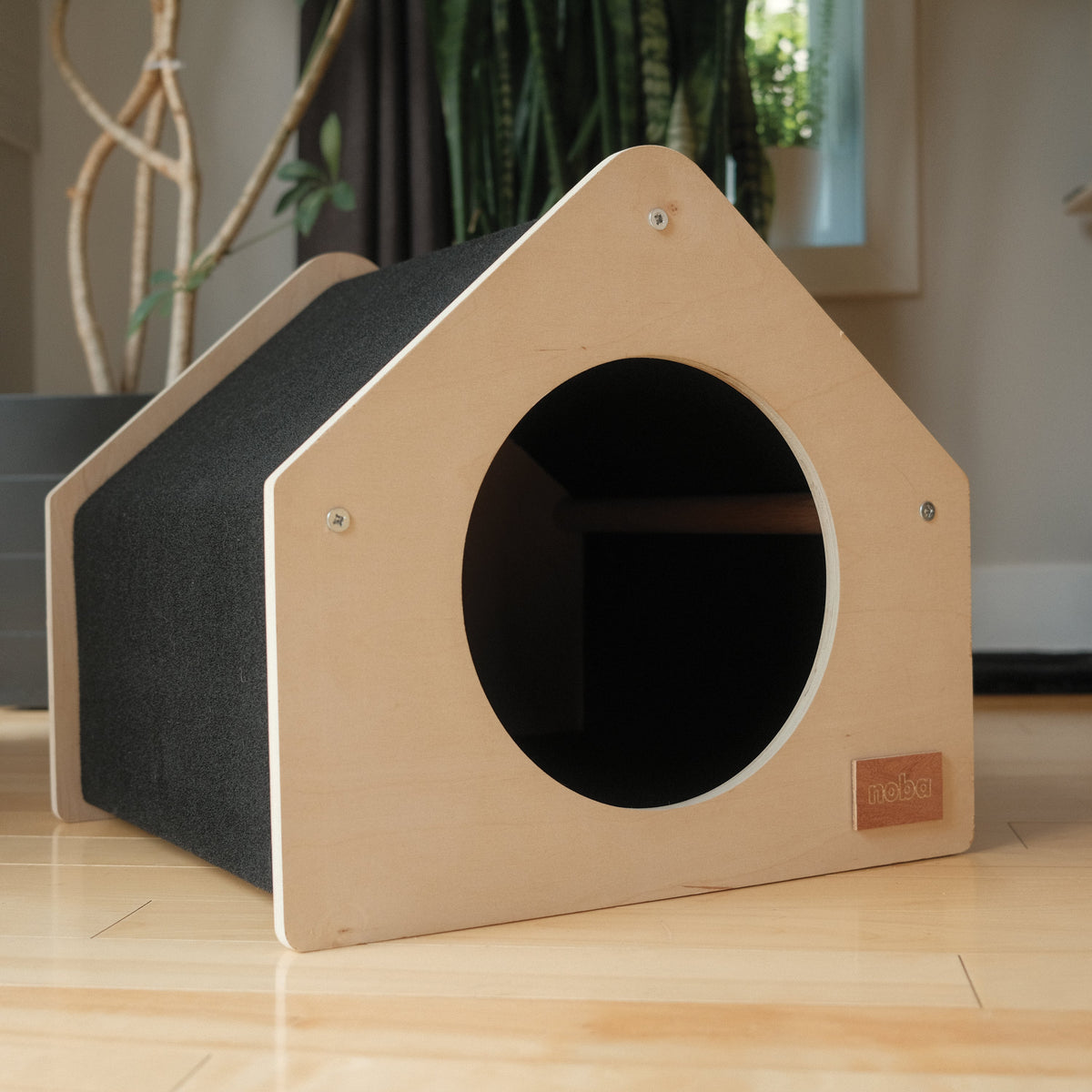 Wooden pet house with a circular entrance on a wooden floor.