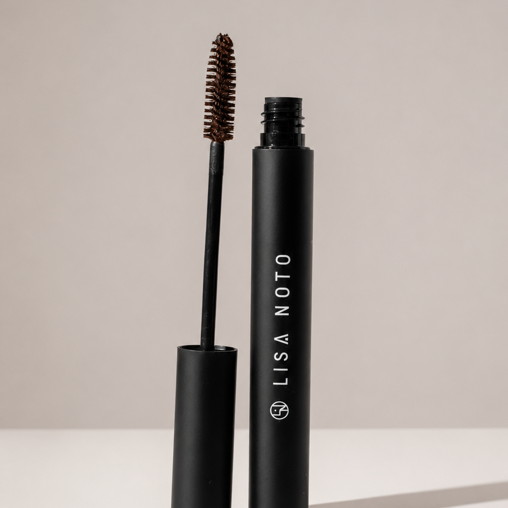 Lisa Noto black mascara shown with the wand removed and standing upright next to the open tube on a clean white surface against a light gray background.