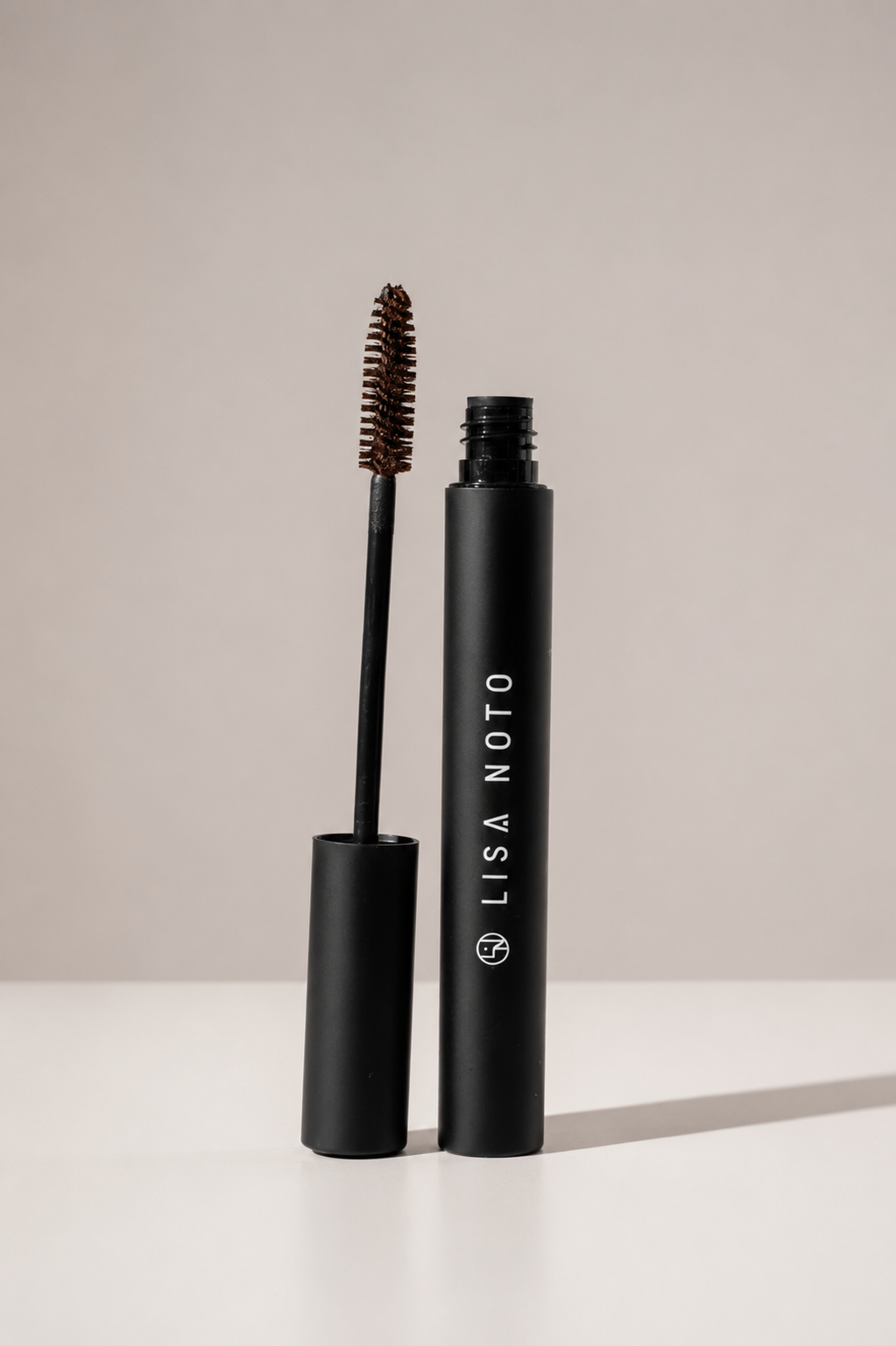 Lisa Noto black mascara shown with the wand removed and standing upright next to the open tube on a clean white surface against a light gray background.