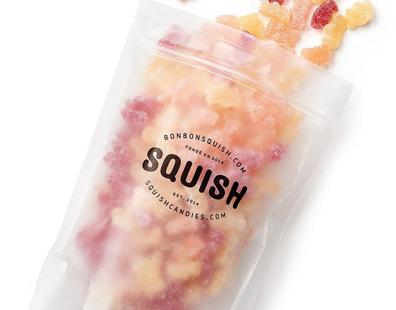 Squish gummy bears spilling out of a clear bag on a white background