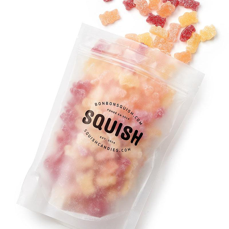 Squish gummy bears spilling out of a clear bag on a white background