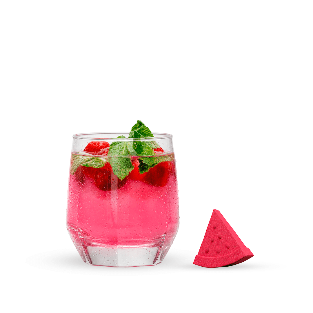 Glass of pink drink with raspberries and mint leaves, accompanied by a watermelon slice on a white background
