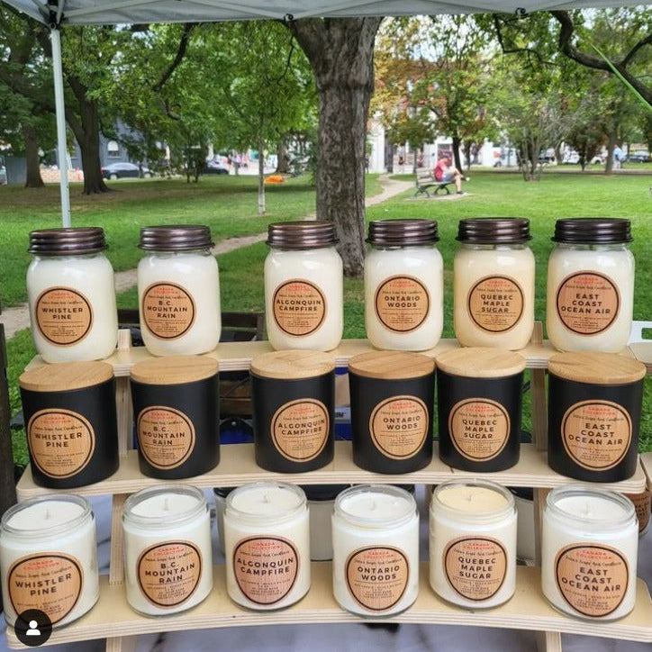 Assorted candles on a wooden stand outdoors with trees and grass in the background