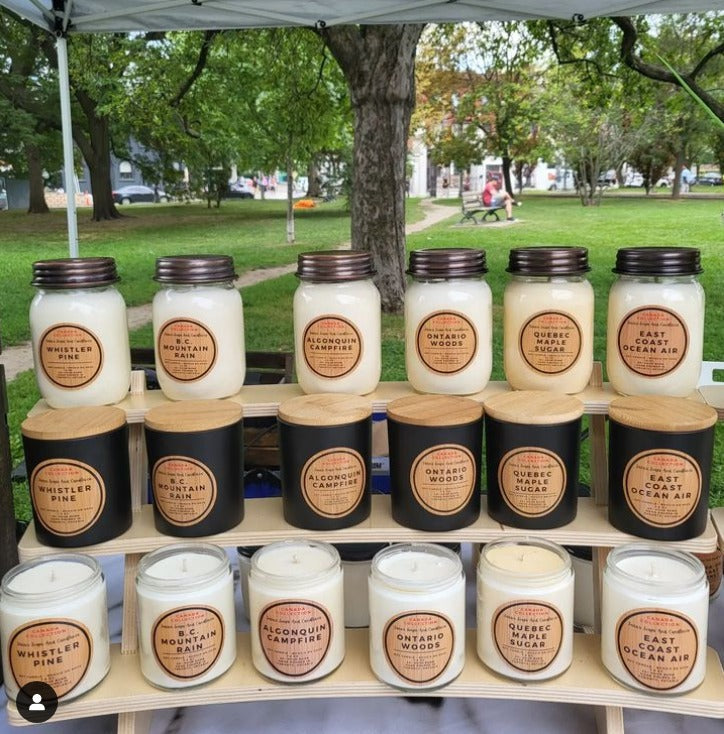 Assorted candles on a wooden stand outdoors with trees and grass in the background