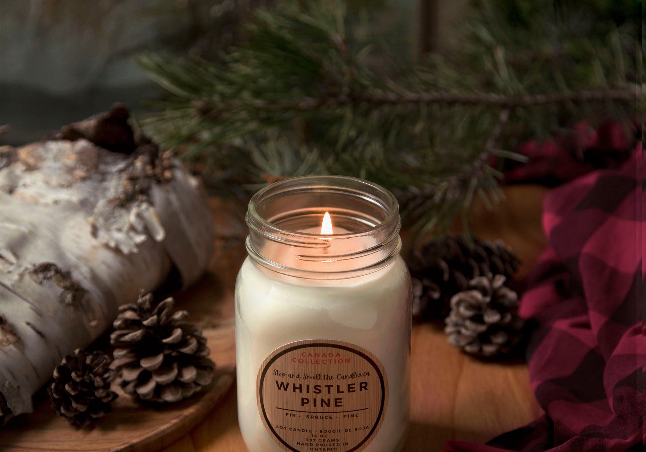 Candle in a mason jar labeled 'Whistler Pine' on a wooden surface with decorative elements.